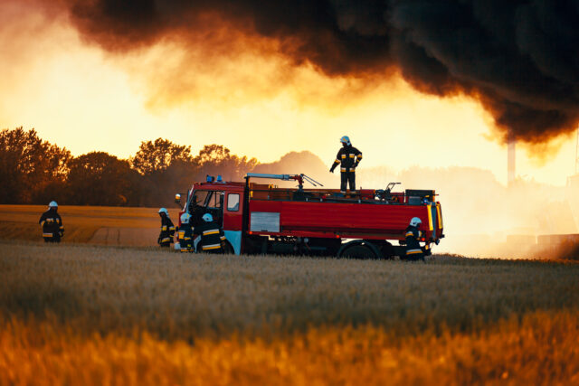 Firefighters with red truck in front of dark smoke from fire